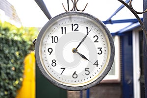 Antique vintage style clock hanging outside, hanging on the wall of a house