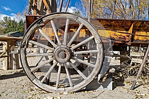 An antique wagon wheel with wooden spokes on a rusty wagon