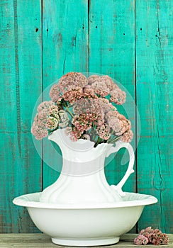 Antique water pitcher and basin with flowers by rustic green wood background