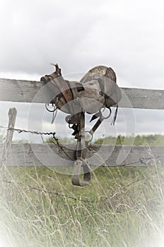 Antique western old fashioned saddle on fence in pasture