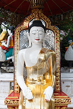 Antique white Buddha statue covered in golden yellow robes at temple in Thailand