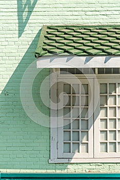 Antique white frame wooden window with light and shadow on the old green pastel brick wall exterior office building or home and