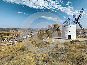 Antique white windmills with blue roof next to a medieval castle