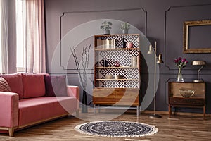 Antique wooden bookcase with decorations in an elegant gray living room interior with a comfortable powder pink sofa