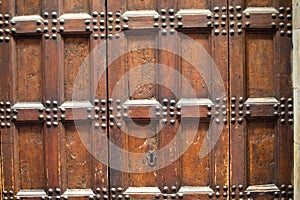 Antique wooden door with metal rivets and keyhole. Close up shot. Aged broun wooden mesh structure. Texture or