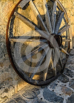 Antique Wooden Wagon Wheel against Stone Wall in Golden Light