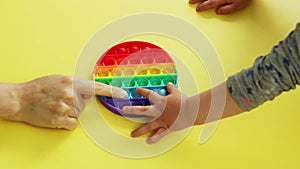 Antistress pop it toy. hands of mom and baby play new popular silicone colorful antistress popit toy for child on yellow