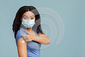 Antiviral immunization. Black lady vaccinated against covid-19, showing arm with plaster, standing on blue background photo