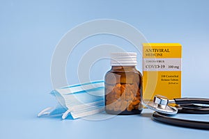 Antiviral medicine COVID-19 tablets in a bottle and a box with a stethoscope and mask on a light blue background. Side view.