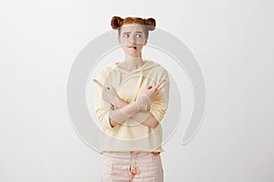 Anxiety keeps intensify. Nervous attractive caucasian redhead with two buns hairstyle pointing in both directions photo