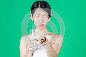 Anxiety stressed young Asian woman holding pills on hands over green isolated background. Medicine and health care concept