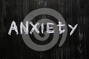 Anxiety word handwritten on black wood background.