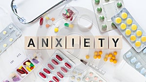 ANXIETY word on wooden blocks on the table. Medical concept with pills  vitamins  stethoscope and syringe in the background