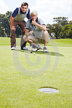 Anxious anticipation of the perfect putt. Two men anxiously watching a golf ball rolling towards the hole on the green.