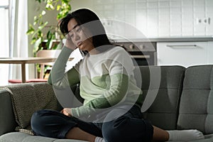 Anxious Asian millennial girl sitting on sofa alone feeling lonely, suffering from monophobia