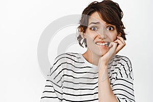 Anxious brunette woman biting fingers, looking scared, frightened about something, look nervous, standing over white