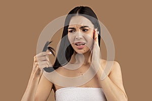 Anxious brunette woman checking her hair, beige background