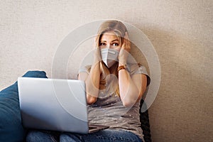 Anxious caucasian girl clutching her head with hands in alarm and looking to her laptop at the horrific numbers of statistics on