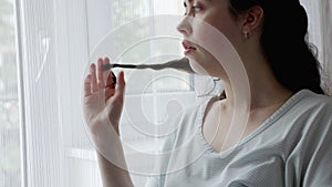 Anxious Caucasian woman curls lock of hair on her finger and lookind at window. Jib shot. Concept of psychological