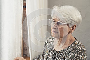 anxious concerned elderly caucasian pensioner wearing glasses and looking uneasily through the window