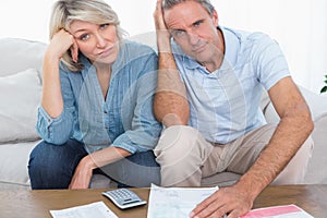 Anxious couple going over bills looking at camera