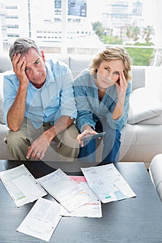 Anxious couple sitting on their couch paying their bills