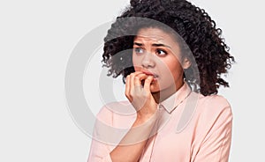 Anxious fearfull African American young woman keeps hand near mouth, feels frightened and scared