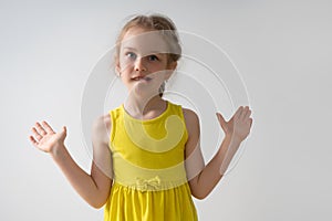 Anxious little girl throwing up her hands in a helpless gesture and biting nervously her low lip. Waist-up studio