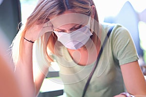 anxious sad woman in medical protective mask sits at table photo