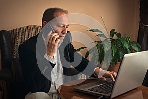 Anxious senior man phoning while working with his laptop at home