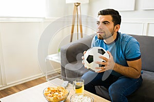 Anxious sports fan holding a soccer ball on the sofa