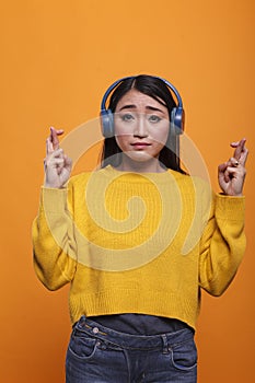 Anxious stressed asian woman having crossed fingers before job interview on orange background