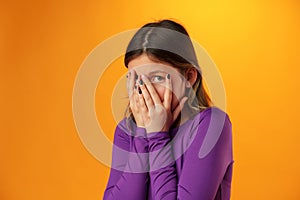 Anxious teen girl looking scared or worried on yellow background