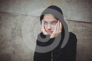 Anxious teenage girl in black hooded jacket standing with hand on face