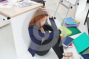 Anxious upset young Asian business woman with hands on head sitting on floor at her in workplace of office.