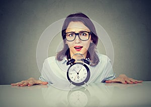 Anxious woman picking from under the table with alarm clock.