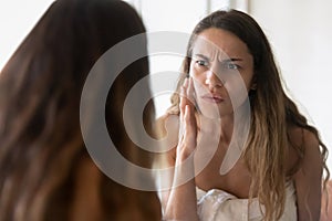 Anxious young woman look in mirror worry about skin problems