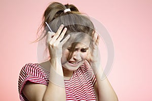 Anxious young woman with medical pregnancy test on pink studio background, disappointed girl cry in stress, concept of unplanned