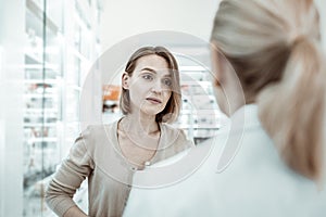 An anxiously looking picky woman attentively listening to the pharmacist.