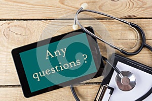 Any questions ? - Workplace of a doctor. Tablet, stethoscope, clipboard on wooden desk background. Top view