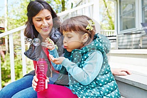 Anything is fun when we do it together. a mother watching her daughter blow bubbles outside.