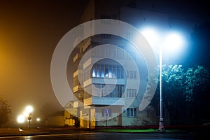 Apartment block on empty night city street covered with fog