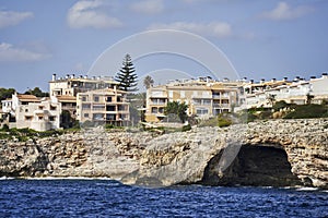 Apartment blocks with holiday apartments behind a breakwater on the steep rocky coast of Mallorca