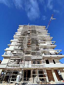 Apartment building construction site with scaffolding and a crane with a blue sky background
