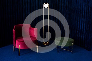An apartment with a comfortable red velor armchair, a minimalist floor lamp and a green pouffe in a room with dark blue velvet