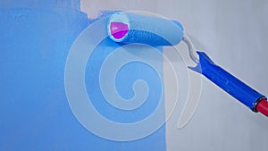 Apartment interior and renovation, closeup paint roller with blue paint moves on white wall in slow motion