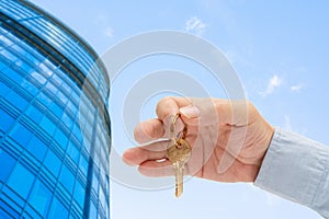 Apartment key in a man`s hand. Brass house door lock key. Modern building, view from below. Architecture in modern city.