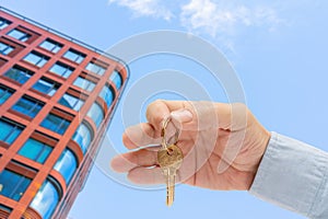 Apartment key in a man`s hand. Brass house door lock key. Modern building, view from below. Architecture in modern city.