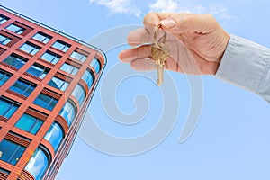 Apartment key in a man`s hand. Brass house door lock key. Modern building, view from below. Architecture in modern city.