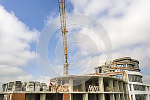 Apartment or office tall building under construction. Brick walls, glass windows, scaffolding and concrete support pillars. Tower